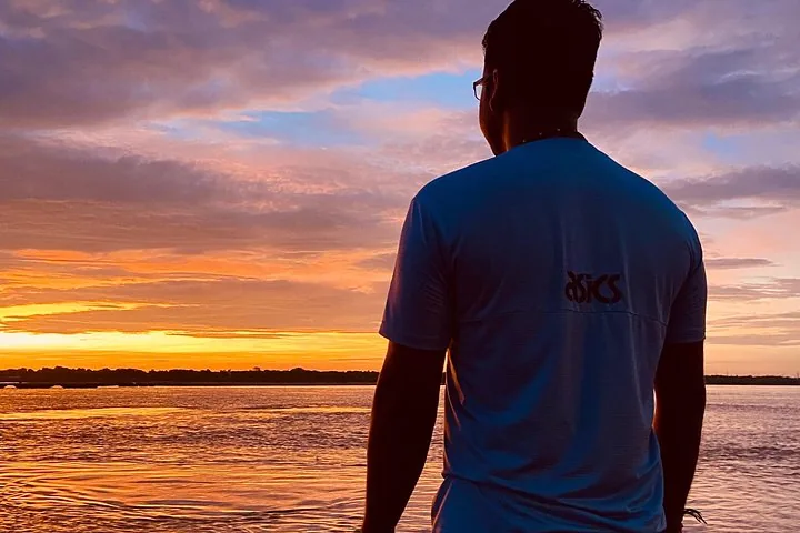 Ein Mann blickt bei einem wunderschönen farbenfrohen Sonnenuntergang über den Ganges.